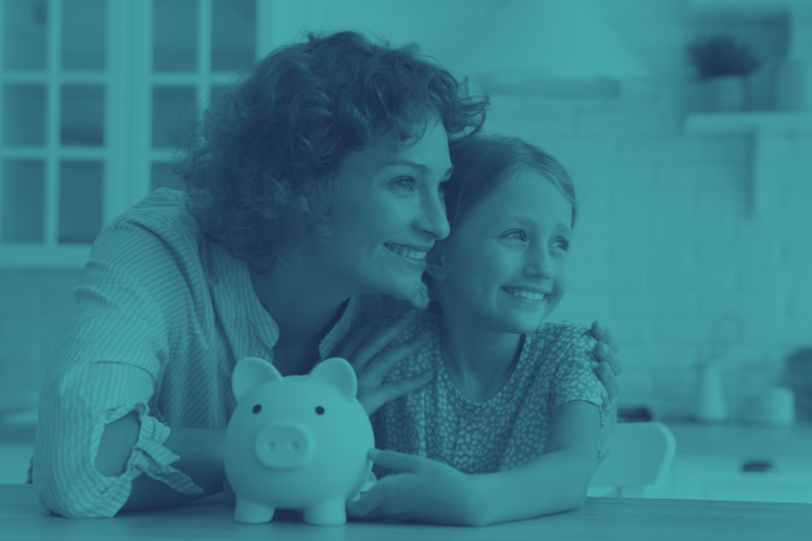 Mother and daughter smiling while saving money with a piggy bank on the kitchen table.