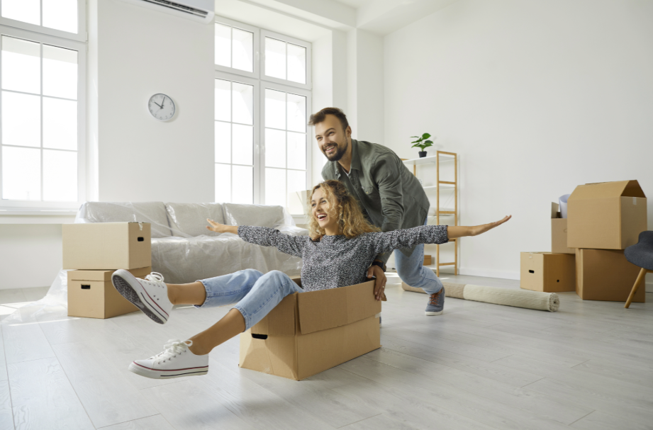 Young couple celebrating moving into new home, playing with cardboard boxes in bright living room