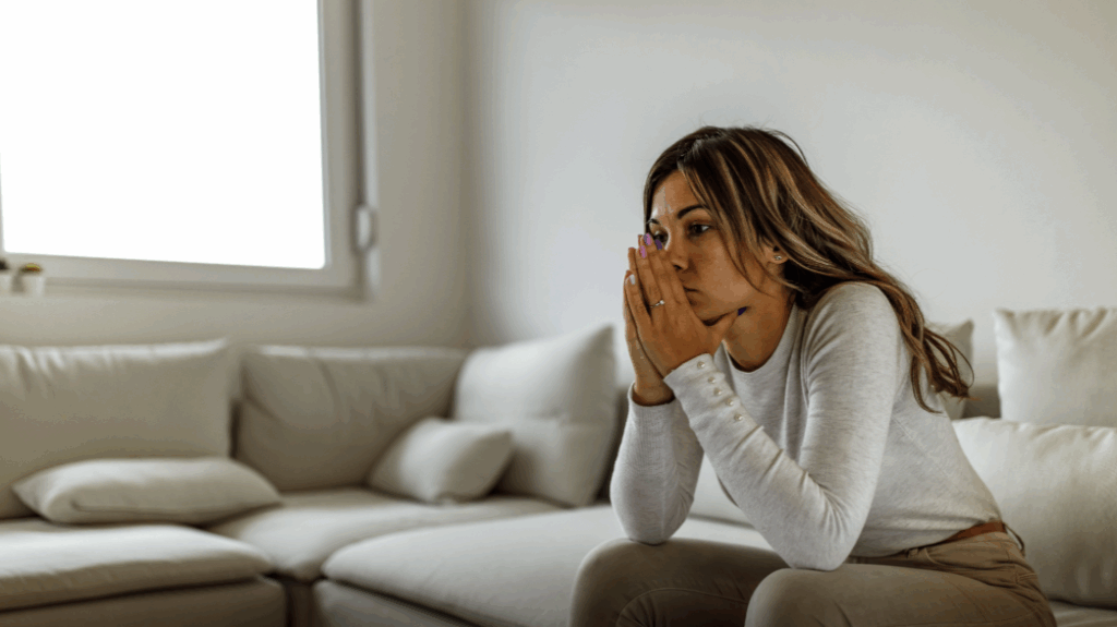 Woman sitting thoughtfully on a couch, reflecting after separation or divorce, symbolising emotional and financial decision-making.